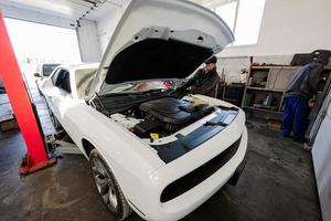 Mechanic in service repair station working with muscle car.  Man worker with open hood of vehicle. photo