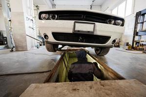 Mechanic in service repair station working with muscle car.  Inspects the running part of the wheel. photo