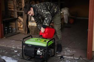 Man wear in military jacket pour gasoline from canister in portable mobile backup standby generator. photo