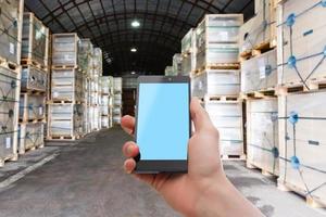 Hand holding smartphone against shelves with boxes in warehouse photo