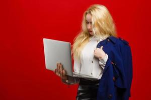 Beautiful young stylish female blogger and laptop - student or accountant posing on a red background. Advertising space photo