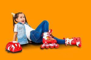 un adorable niño en edad preescolar sonriendo aunque caído mientras aprende a patinar. sobre un fondo naranja. foto