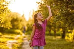 niña caucásica de cinco años que sopla pompas de jabón al aire libre al atardecer - infancia feliz y despreocupada. foto