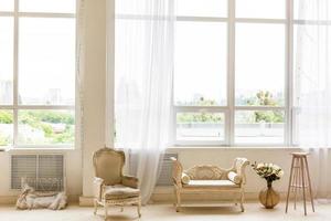 Pouf and gray armchair in spacious living room interior with plants and sofa near wooden table photo