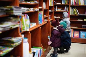 Little cute baby in jacket reaching a book from bookshelf at the library. Learning and education of european kids. photo