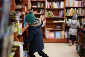 niño con chaqueta alcanzando un libro de la estantería de la biblioteca. aprendizaje y educación de los niños europeos. foto