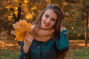 la joven sonriente en el parque mantiene el cabello con una mano mientras que la otra sostiene las hojas foto