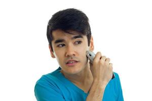 wonderful young guy with black hair shaves his beard shaving machine and looks toward close-up photo