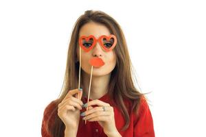 a young girl in a red shirt posing on camera holding hands near the face paper glasses and sponges for photos