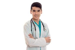 retrato de un joven y apuesto doctor moreno con uniforme blanco con estetoscopio mirando a la cámara y sonriendo aislado en un fondo vacío foto