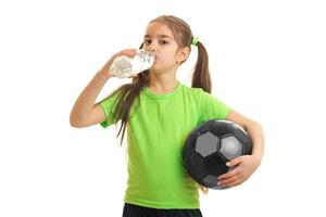 little girl in green uniform playing soccer with ball and drinks water photo