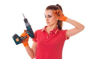 portrait of young attractive brunette building woman in red uniform with drill in hands makes renovation isolated on white background photo