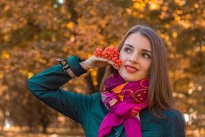 beautiful girl stands in the park looks away and holds a sprig of Rowan in his hand photo