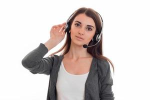 hermosa joven con auriculares con micrófono mira a la cámara y sostiene su mano cerca de la oreja foto