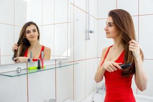 young beautiful girl in a red vest combing her hair in front of a mirror photo