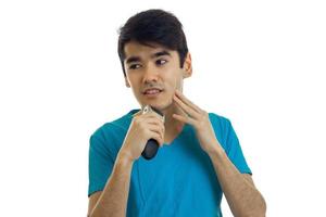 chico lindo joven con cabello negro mira hacia otro lado y se afeita una recortadora de barba foto