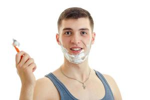 Portrait of a young smiling guy with foam on his face which looks straight and holding a razor photo