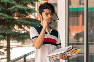 cute guy stands on a street holding a book and dress glasses photo