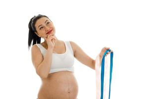 studio portrait of young pregnant brunette woman with blue tape in her hands isolated on white background photo