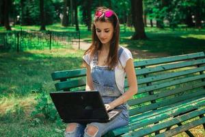 chica joven alegre que usa una computadora portátil en un banco foto