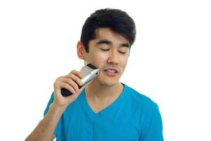 charming young guy in the blue shirt closed his eyes and shaves a beard trimmer is isolated on a white background photo
