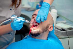 un joven agradable trata sus dientes en un consultorio dental del médico foto