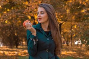 hermosa chica parada en el parque mira hacia otro lado y mantiene la manzana en la mano foto