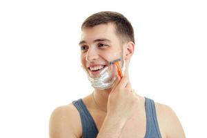 Portrait of a beautiful, cheerful guy who turned his head toward laughs and shaves his beard with foam on his face photo