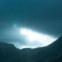 Square photo of dramatic rays of light pushing up through clouds