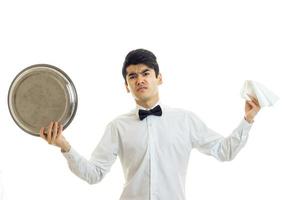 el joven camarero enojado con una camisa blanca sosteniendo una bandeja de vajilla y servilleta foto