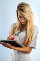 Vertical photo of young adult nurse with blonde hair writes