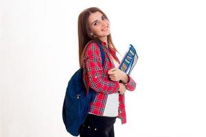 linda jovencita con una camisa a cuadros y un maletín en la espalda sonriendo y sosteniendo una carpeta foto
