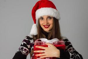 mujer en suéter cálido y sombrero de santa con regalo rojo foto