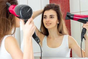 fun pretty girl dries hair standing in front of a mirror photo