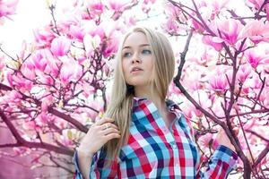 chica rubia de ensueño mirando hacia el lado cerca de los árboles florecientes de primavera foto