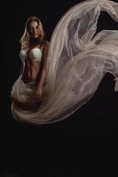 Vertical photo of sexual blonde woman in white bra and flying fabric