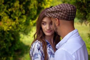 un joven elegante mira a su hermosa chica cuando sonríe y mira hacia el parque verde foto