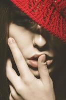 Close up portrait of woman with red hat and hand near lips photo