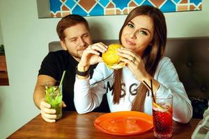 pareja posando en la cafetería con hamburguesas y cócteles foto