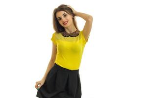 a charming young girl in a yellow t-shirt and skirt smiles and holds her hand near hair photo