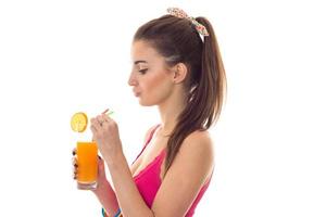profile of young beautiful brunette girl in pink shirt drinks orange cocktail and smiling on camera isolated on white background photo