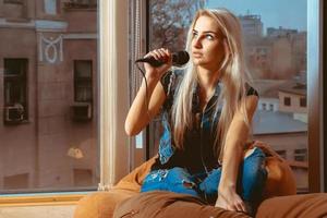 linda jovencita rubia cantando karaoke con micrófono y mirando hacia otro lado foto