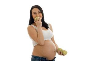 young pregnant brunette girl eats green apples isolated on white background photo