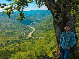 guy posing near tree with view on mountains and river photo