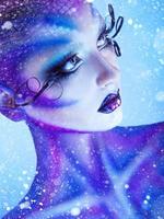 Vertical portrait of young adult girl with creative body art looking away with snow on background photo