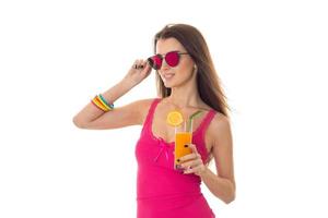 a young girl in a pink shirt and colored glasses looks to the side and holding a glass of juice photo