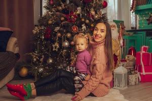 retrato de mamá feliz con su pequeña hija en el árbol de navidad foto