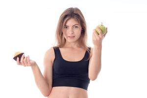 Slim young girl in black top holding Apple and a cupcake is isolated on  white background photo