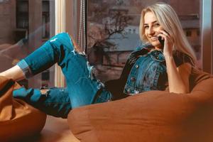 Blonde young woman talking phone and smiling on camera in casual clothes photo