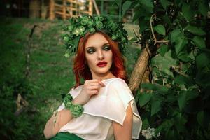 serious woman with wreath on head posing on tree photo